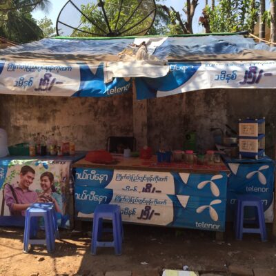 Bod utendørs i Myanmar med reklameposters for Telenor.