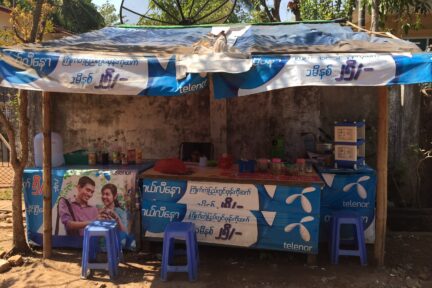 Bod utendørs i Myanmar med reklameposters for Telenor.