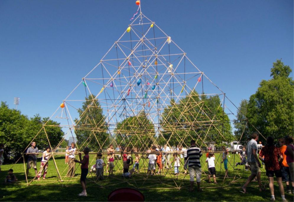 en gruppe mennesker som bygger en pyramide av bambuspinner og gummistrikker sammen. Dette krever ikke mye forkunnskap eller ferdigheter, bare mye samarbeid og vilje til å utvikle noe sammen