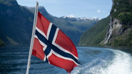 bilde av et norsk flagg som vaier over en fjord med fjell i bakgrunnen