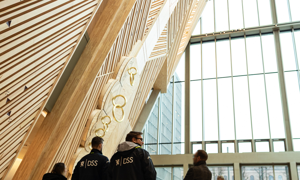 En liten gruppe ansatte i et stort rom tilhørende nytt regjeringskvartal. På et par av de ansatte ser man tydelig logo som leser "DSS".