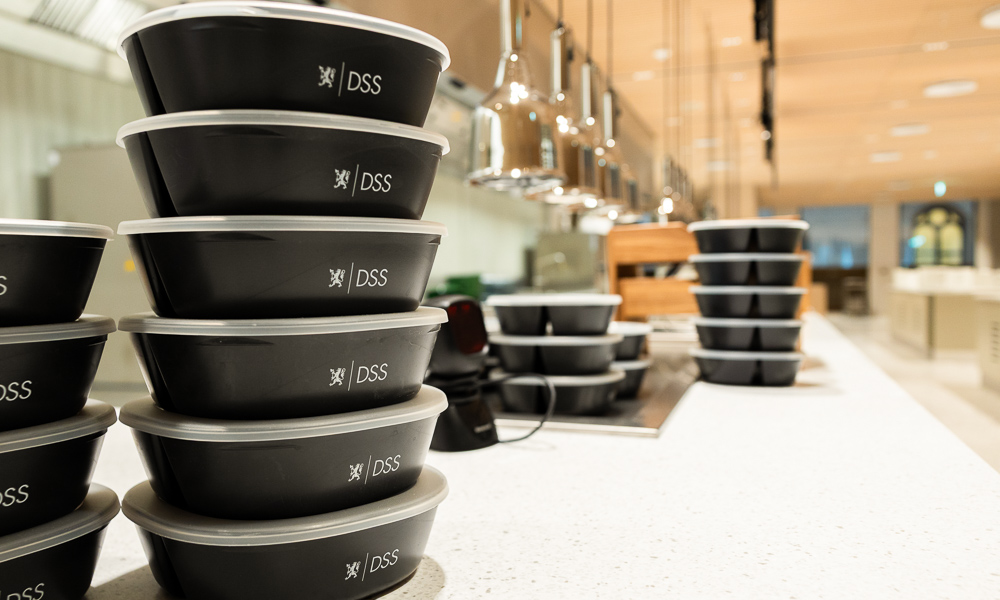 Et tårn av stablede matbokser i en kantine. På matboksene finner man tekst som leser "DSS".