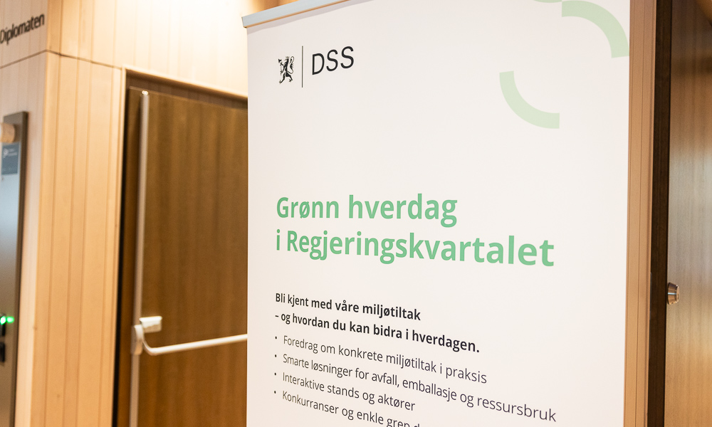 En roll-up plakat med tydelig DSS logo i venstre hjørne. På plakaten leser man teskten "Grønn hverdag i Regjeringskvartalet".