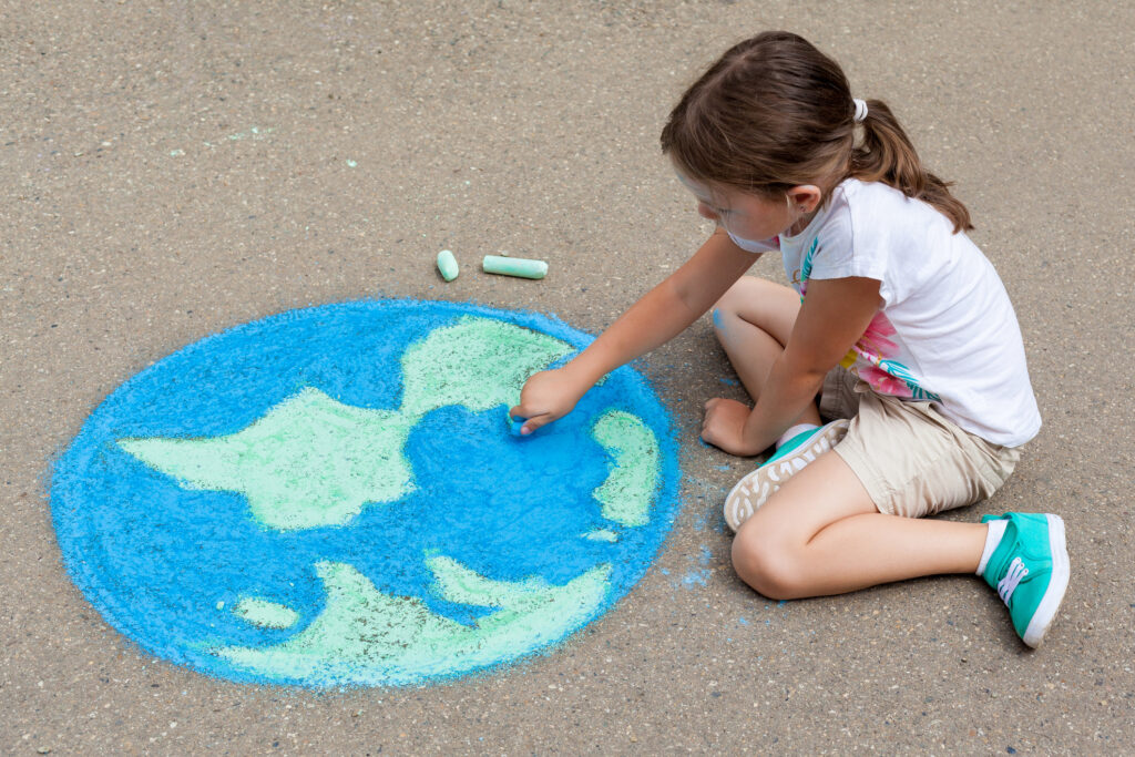 the child girl draws a planet of the world with colored chalk on the asphalt. Children's drawings, paintings and concepts. Education and art, be creative when you return to school.  earth, Peace day