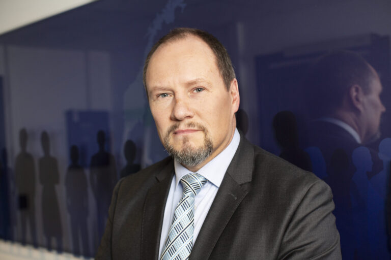 Direktør i SKM Gudmund Gjølstad stående foran blått skilt