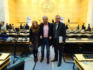 Tre personer står samlet i en sal. Det er flere personer som er bak dem.