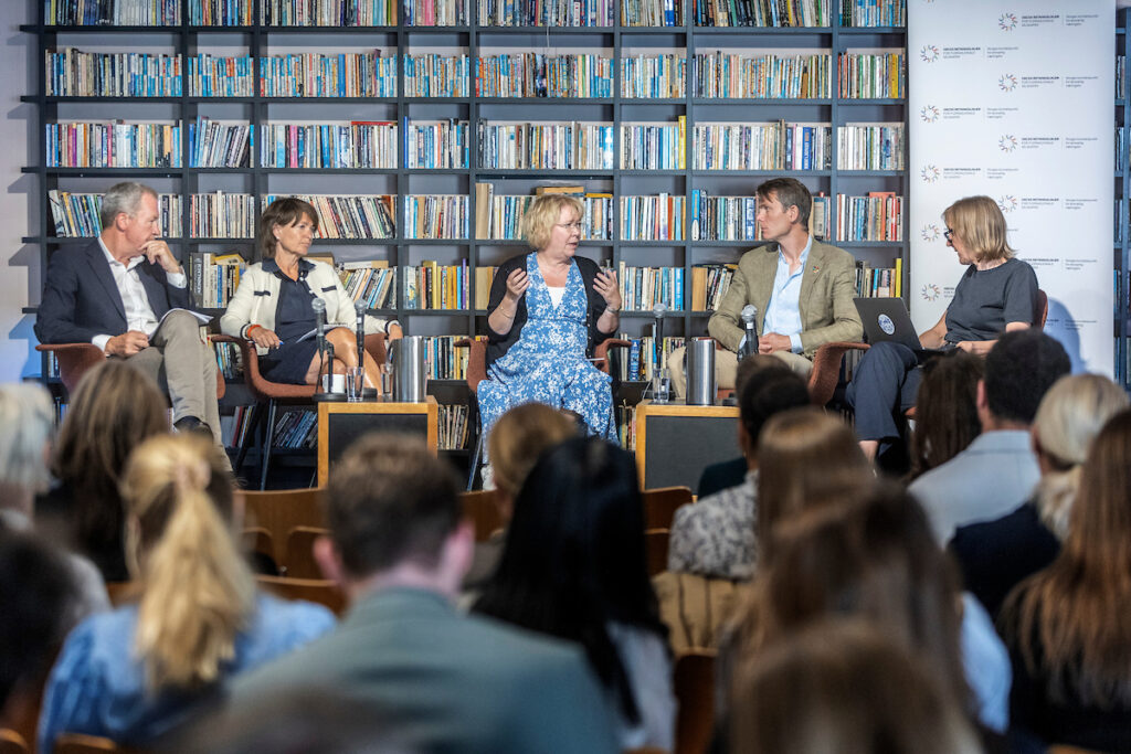 Paneldiskusjon med fem personer på en scene.