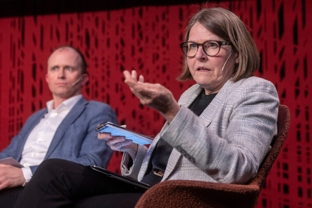 Dame deltar i paneldebatt. Sitter i en stol og snakker. En mannlig paneldeltaker sitter til venstre.