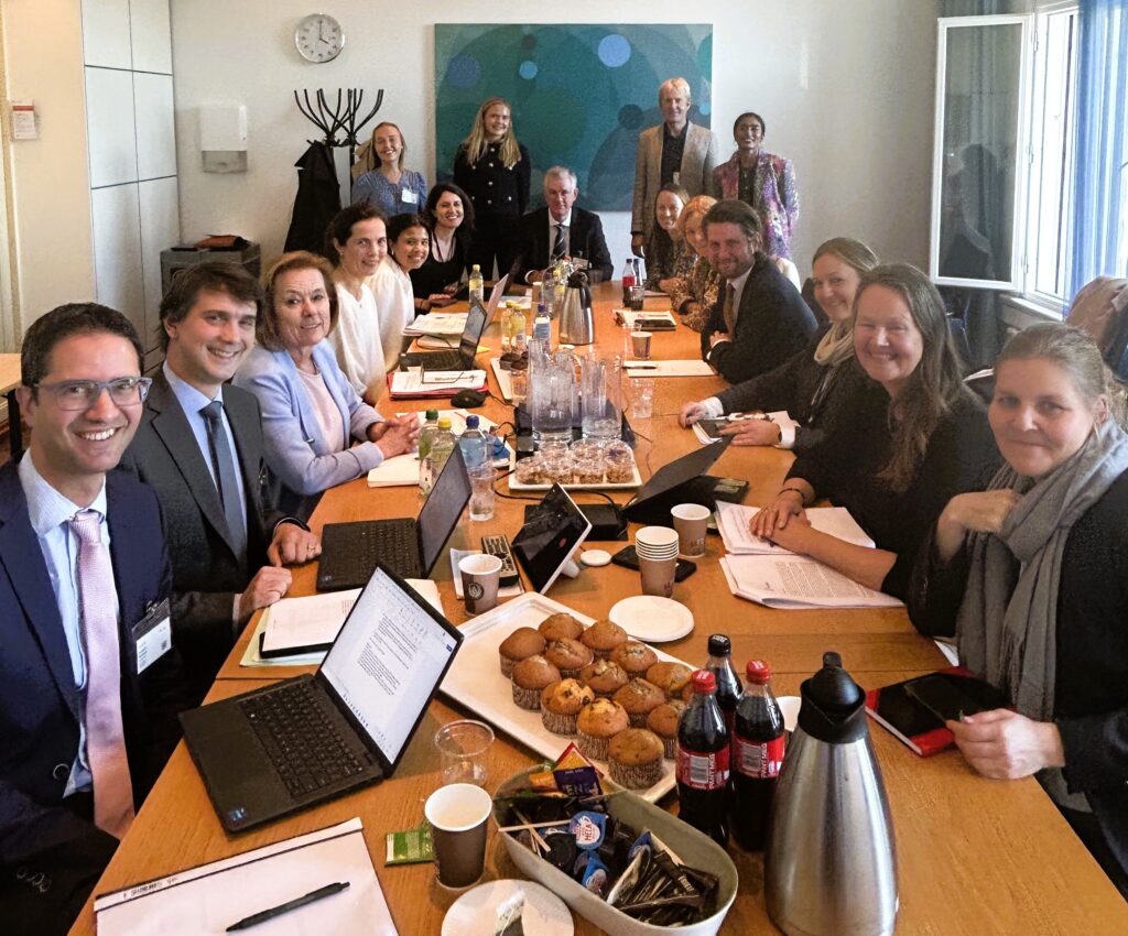 12 damer og 5 menn rundt et møtebord, alle med blikket vendt mot fotografen