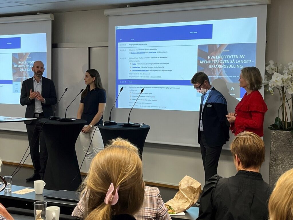To menn og to kvinner i diskusjon står foran et lerret